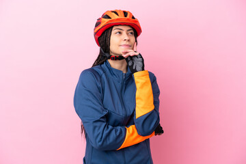 Teenager cyclist girl isolated on pink background having doubts while looking up