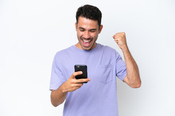 Young handsome man over isolated white background using mobile phone and doing victory gesture