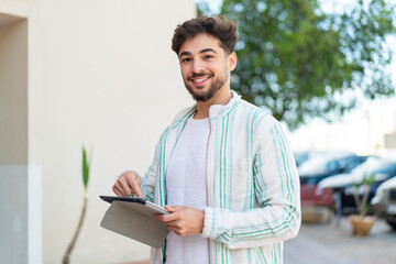 Handsome Arab man at outdoors touching the tablet screen with happy expression