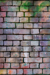 The brick wall is stained with multi-colored paints. The wall is covered with graffiti.