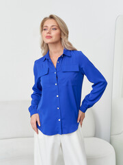 Model in studio poses elegantly with a vibrant blue shirt against a modern backdrop