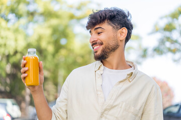 Young Arabian handsome man holding an orange juice at outdoors with happy expression