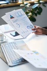 Vertical shot of unrecognizable male specialist looking through papers with financial graphs and...