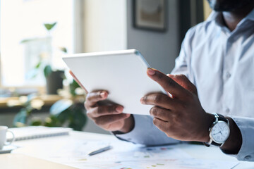 Closeup of hands of unrecognizable black male man holding digital tablet, using it for making presentation at work in office