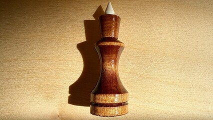  wooden chess king piece with white crown tip on bright wood background ideal for game themed web design, print materials, branding, and illustration