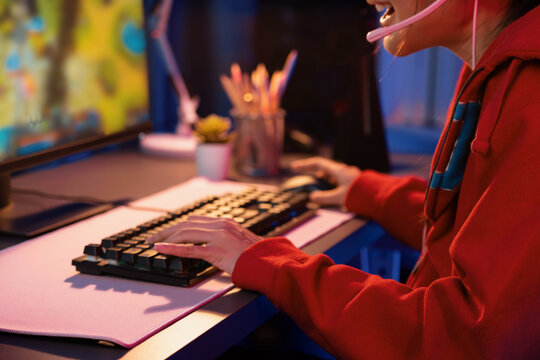 Host channel of young beautiful Asian gaming streamer playing fighting Moba at battle arena game on pc screen with multiplays, wearing pastel headphone at neon digital light modern room. Stratagem.
