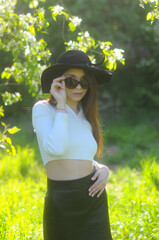 young girl walking in a summer park in a black hat in a white blouse and skirt