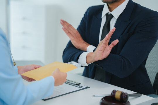 Lawyer showing stop hand gesture, refusing to accept bribe or illegal money inside courtroom with gavel and themis statue