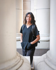 Multiethnic nursing student standing outside and academic building with a backpack on and looking at the camera. Attractive female medical student photo