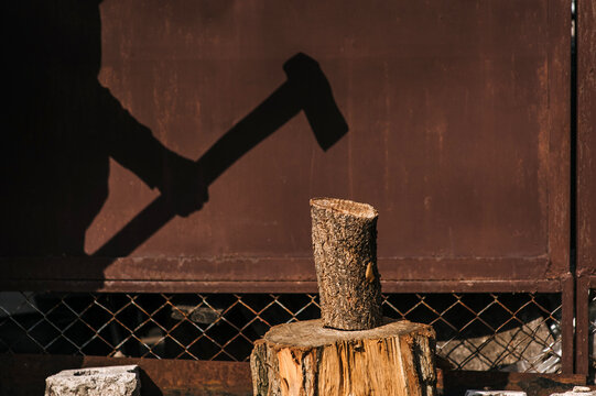 Photograph of silhouette, shadow on wall of adult male strong lumberjack chopping log on stump with axe in forest against wall outdoors.