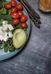 Veganism Concept. Fresh vegetables and herbs on a dark surface top view. avocado, cherry tomatoes, bell peppers, asparagus, parsley and grain mustard. 