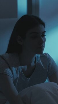Vertical video. Night anxiety. Insomnia disorder. Tired sad lonely depressed sleepy overthinking woman sighing yawning in bed late in dark bedroom.
