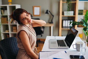 Stressed asian freelancer woman suffering neck pain while working remotely from home