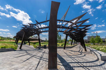A stunning steel sculpture stands in an urban park, casting intricate shadows on the ground as...