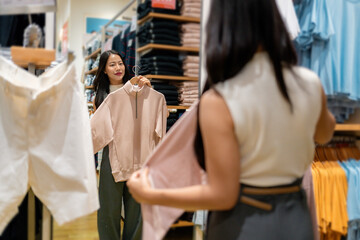 Customer holding a pink sweater in a clothing store, looking at her reflection in a mirror