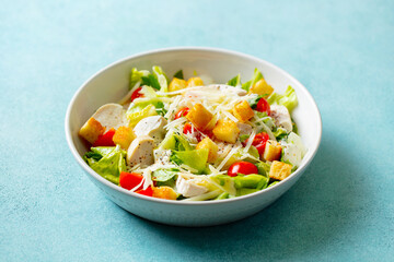 Caesar salad with chicken in a white bowl. Blue background. Close up.