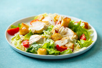 Caesar salad with chicken in a white plate. Blue background. Close up.