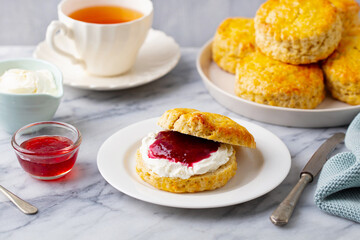 Scones with jam, clotted cream and cup of tea on marble table. Grey background. Close up.