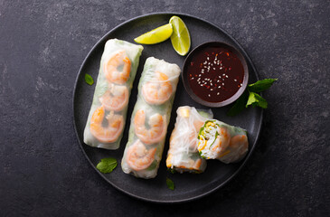 Spring rolls with shrimps and vegetables with spicy soy sauce on a black plate. Dark grey background. Close up. Top view.