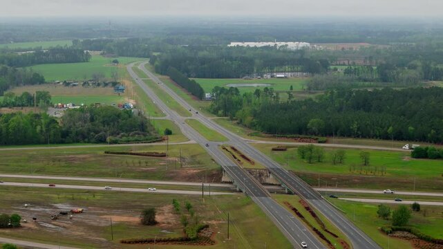 The arial drone view along the highway with intersections and beautiful green suburbs. Wide aerial drone view. 