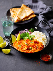 Indian shrimp curry served with basmati rice and naan. The dish is garnished with lemon wedges and fresh cilantro, accompanied by sliced onions for a lavish presentation.
