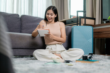 Asian woman writing on a notebook planning next trip sitting on the floor at home