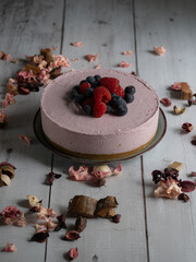 Vertical photograph of a frozen red fruit cake with floral decorations around it in a rustic and romantic setting.
