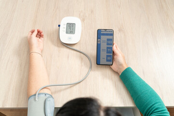 Woman checking blood pressure measurements on a smartphone app, using a wireless tensiometer at home