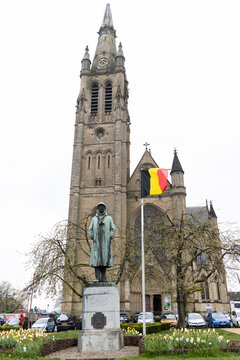 Historical statue in front of a church, displaying a Belgian flag, representing national pride and cultural heritage