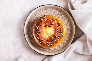 Close up of baked bagel with tomato and quail egg on a plate on the table top view