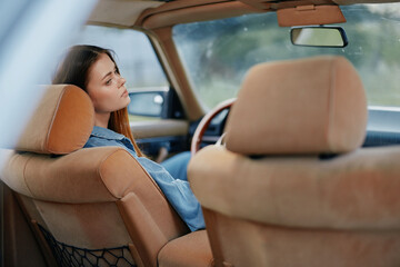 A young woman sitting in a vintage car, lost in thought, captures a moment of nostalgia and...