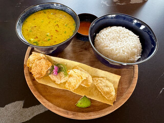 Chicken curry with bowl of rice accompanied with fried wontons. Served on a wooden round try, on a black table.