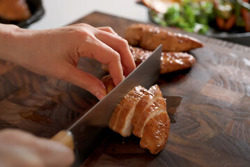 Cutting grilled chicken breast into slices on a wooden cutting board, preparing for a healthy dish