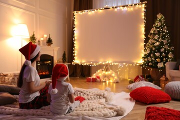 Mother and daughter watching movie using video projector at home. Cozy Christmas atmosphere
