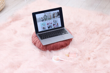 Laptop with fashion blog web site, perfume, face powder and brush on floor indoors