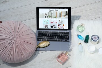 Laptop with fashion blog web site, perfumes, cosmetics and brush on floor indoors, above view