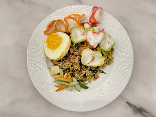 Close up of traditional chicken fried rice with boiled egg and prawn crackers , served on a white plate, on a white marble table.