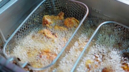 Close-up of crispy fried chicken pieces sizzling in hot oil inside a deep fryer in a Restaurant,...