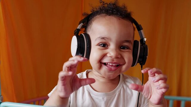 Adorable toddler wearing headphones and making heart gesture with hands, smiling in colorful nursery room