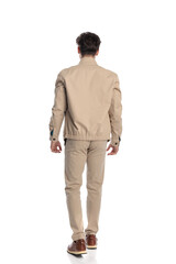 back view of casual young man in beige jacket with chino pants walking