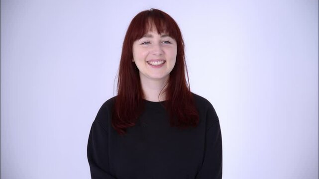 Portrait of a young woman with blue eyes, red hair in a black baize smiling and laughing on a light background.