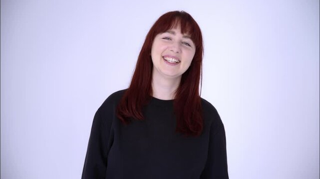 Portrait of a young woman with blue eyes, red hair in a black baize smiling and laughing on a light background.