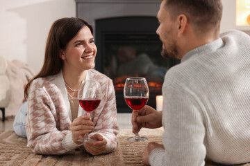 Happy couple with glasses of wine near fireplace on floor at home