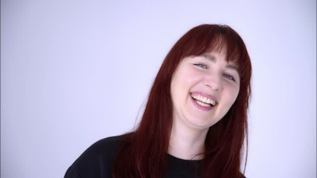 Portrait of a young woman with blue eyes, red hair in a black baize smiling and laughing on a light background.