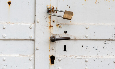 Old White Rusty Door with Padlock and Knob, Close-up of an old, white door covered in rust, featuring a padlock and a metal knob. The weathered look and signs of wear give the door a vintage