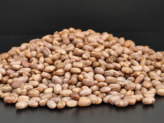 An abundant amount of dry beans scattered on a dark surface, highlighting their natural textures and earthy colors, perfect for food, agriculture, or rustic-themed concepts.