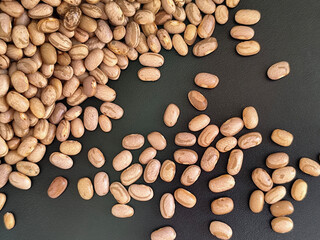 An abundant amount of dry beans scattered on a dark surface, highlighting their natural textures and earthy colors, perfect for food, agriculture, or rustic-themed concepts.