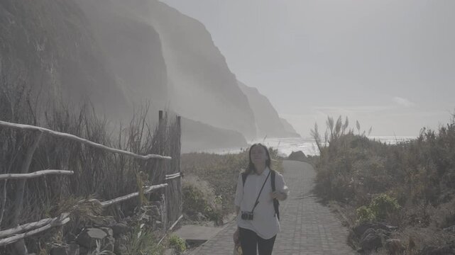 Hiker exploring scenic pathway on Madeira coast surrounded by cliffs and warm fog (SLOG3)