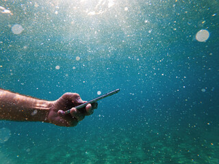 Male diver using smartphone device underwater in deep blue sea during summer holiday vacation