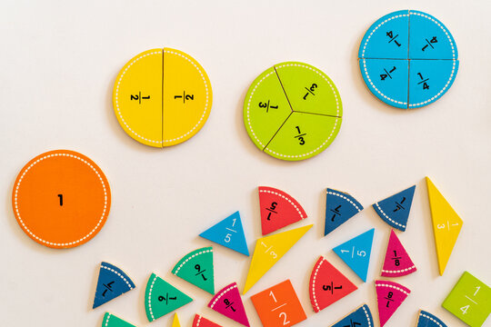 Educational manipulatives for teaching fractions on a white surface with colorful circular and triangular pieces